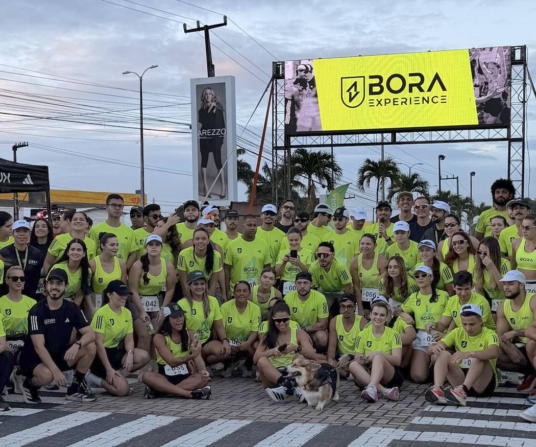 Turma da BORA Natal reunida antes do treino, com o painel BORA Experience ao fundo